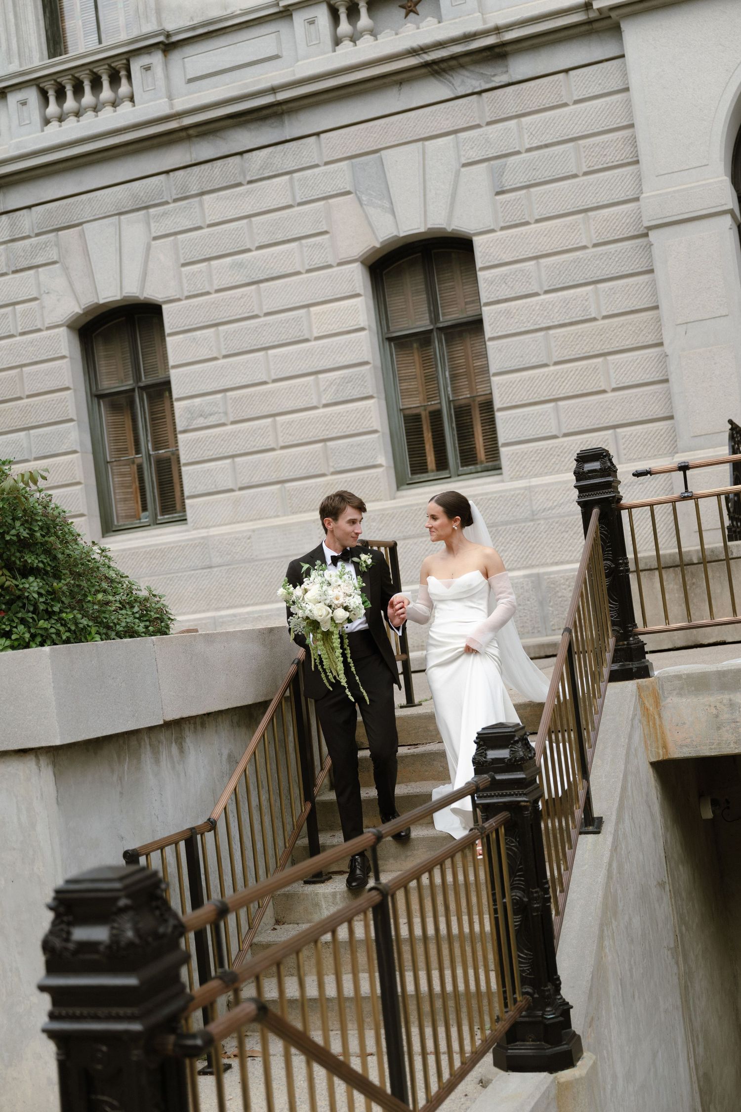 A bride and groom share a romantic moment on stone steps outside a historic building with elegant architecture.