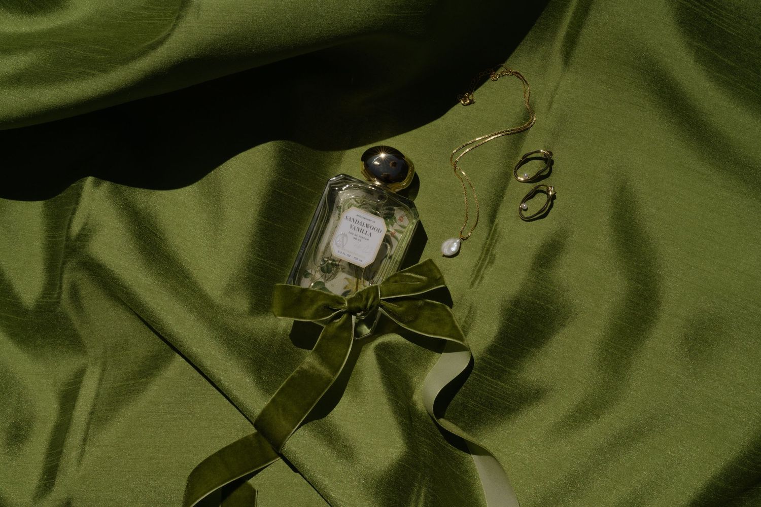 Perfume bottle and rings arranged on olive green silk fabric.