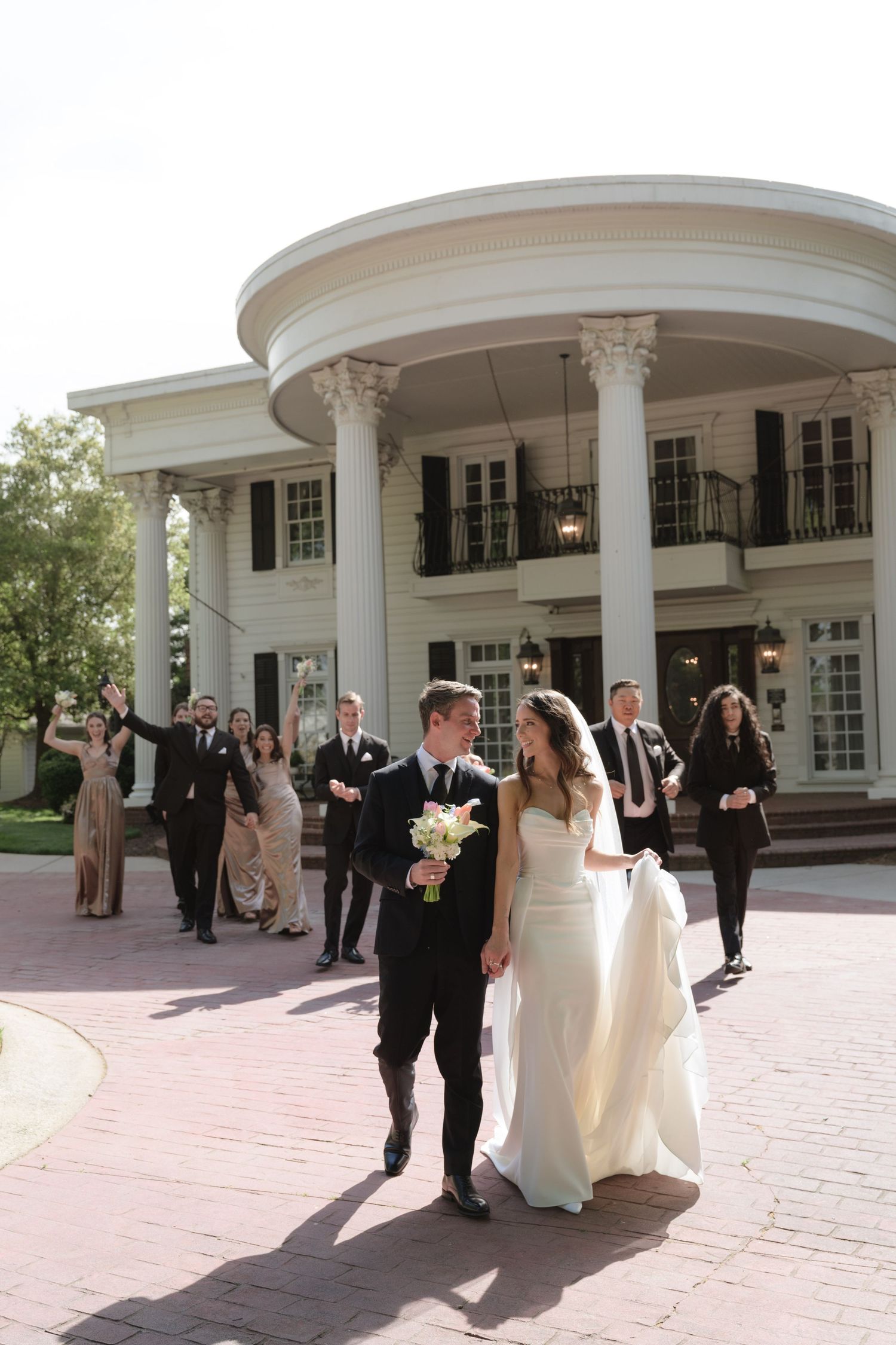 Wedding party gathered outside a grand white columned mansion with classical architecture.