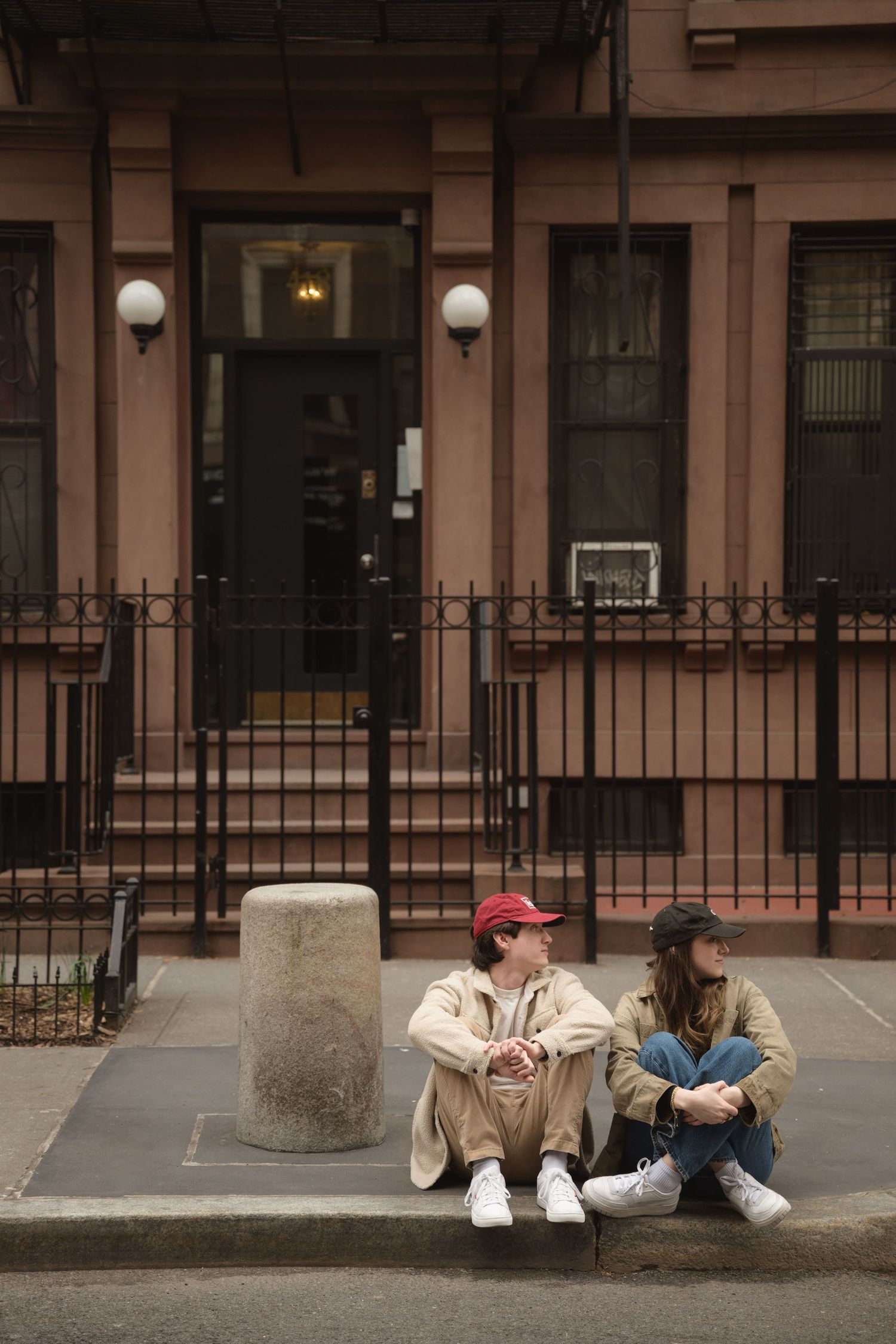 Two people sitting and lounging against building exterior in casual poses.