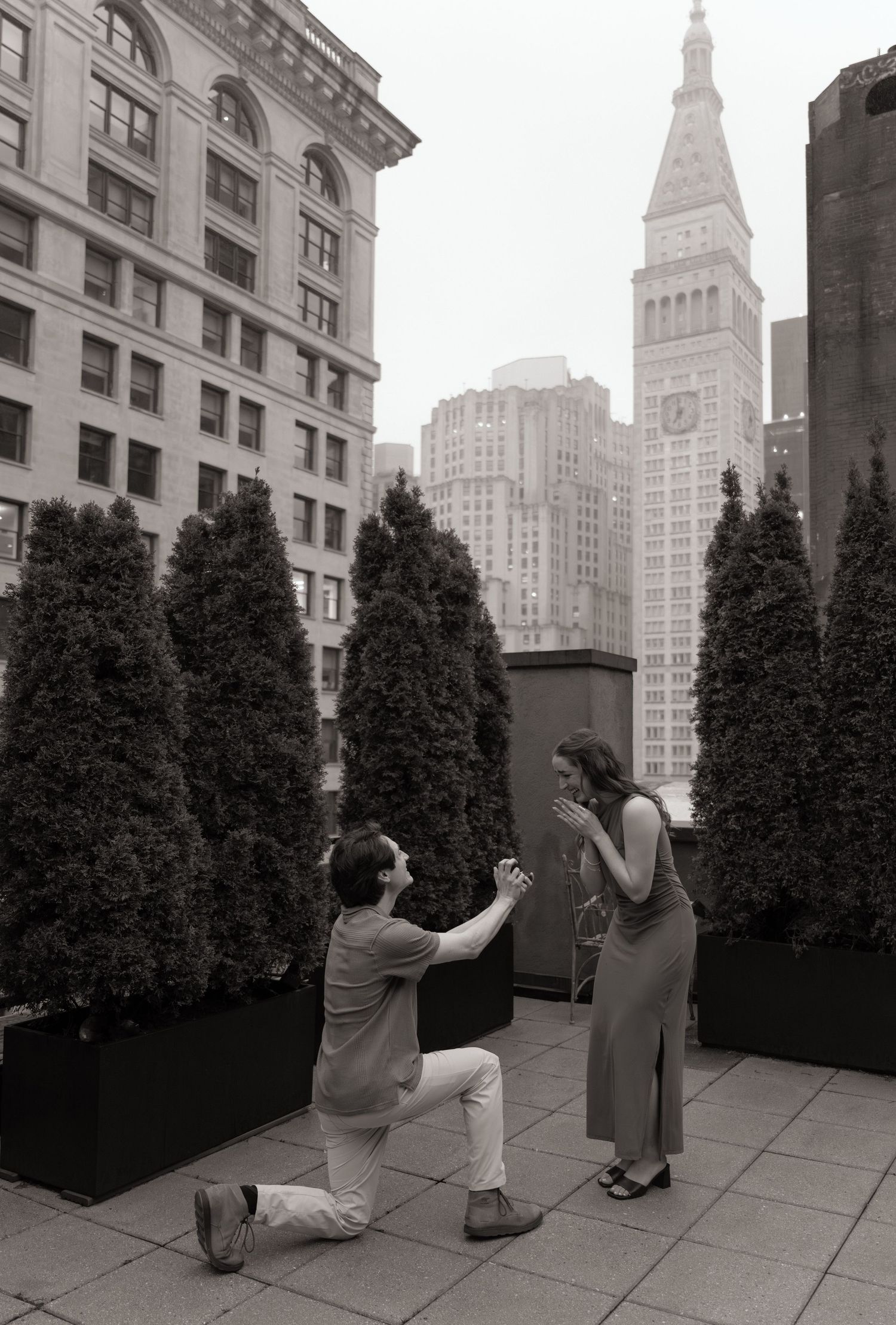 A black and white proposal scene on a Manhattan rooftop with architectural details.