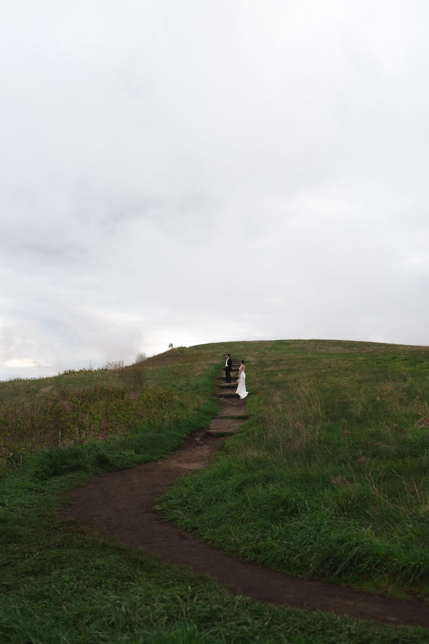 A winding dirt path leads up a grassy hillside under cloudy skies.