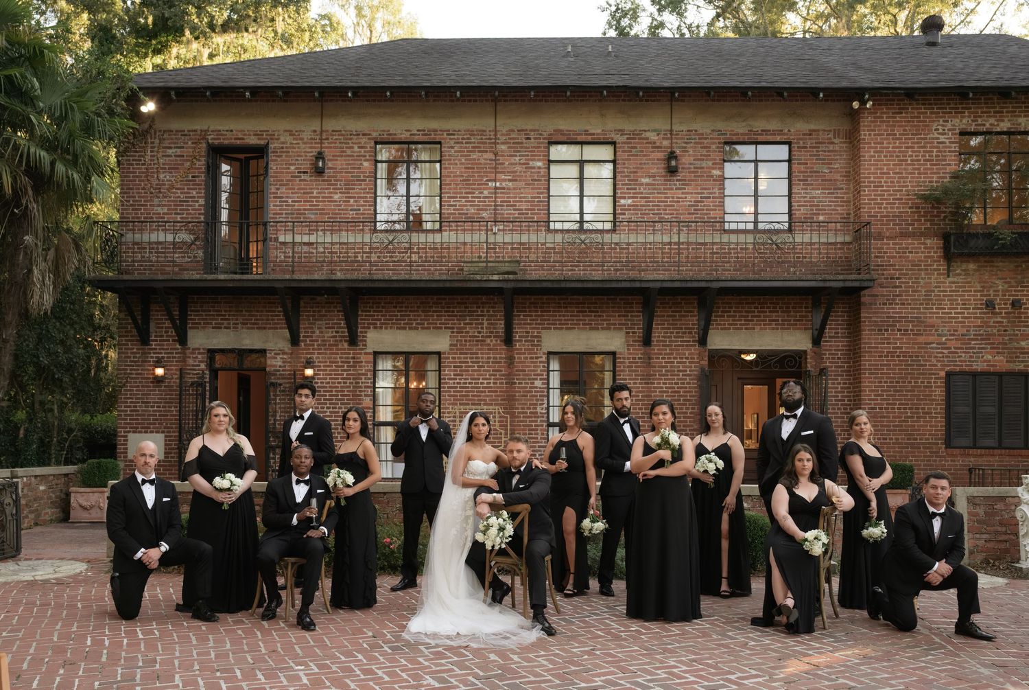 A wedding group portrait session arranged in front of a rustic brick building facade.