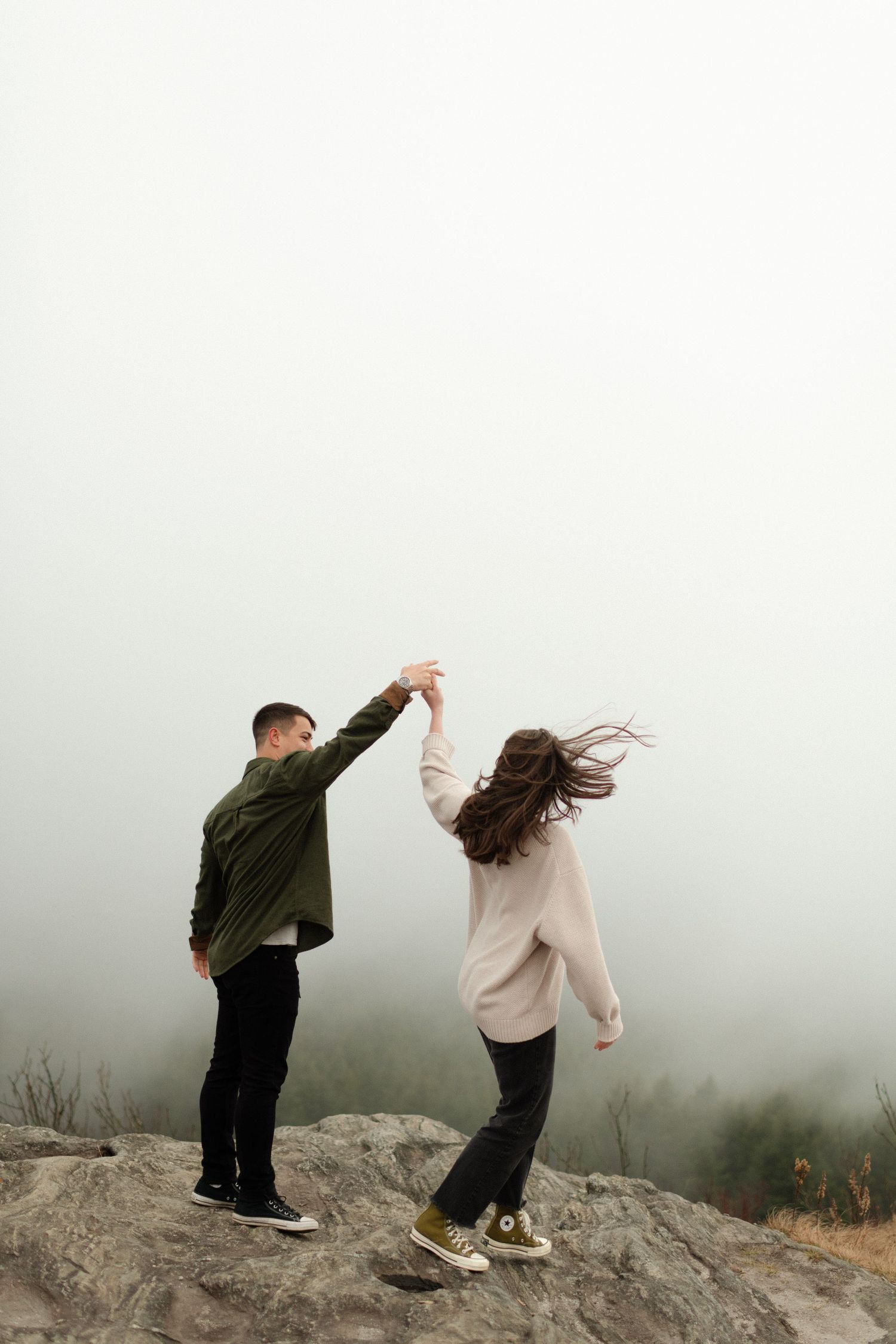 A playful couple dancing together on a foggy mountain summit.