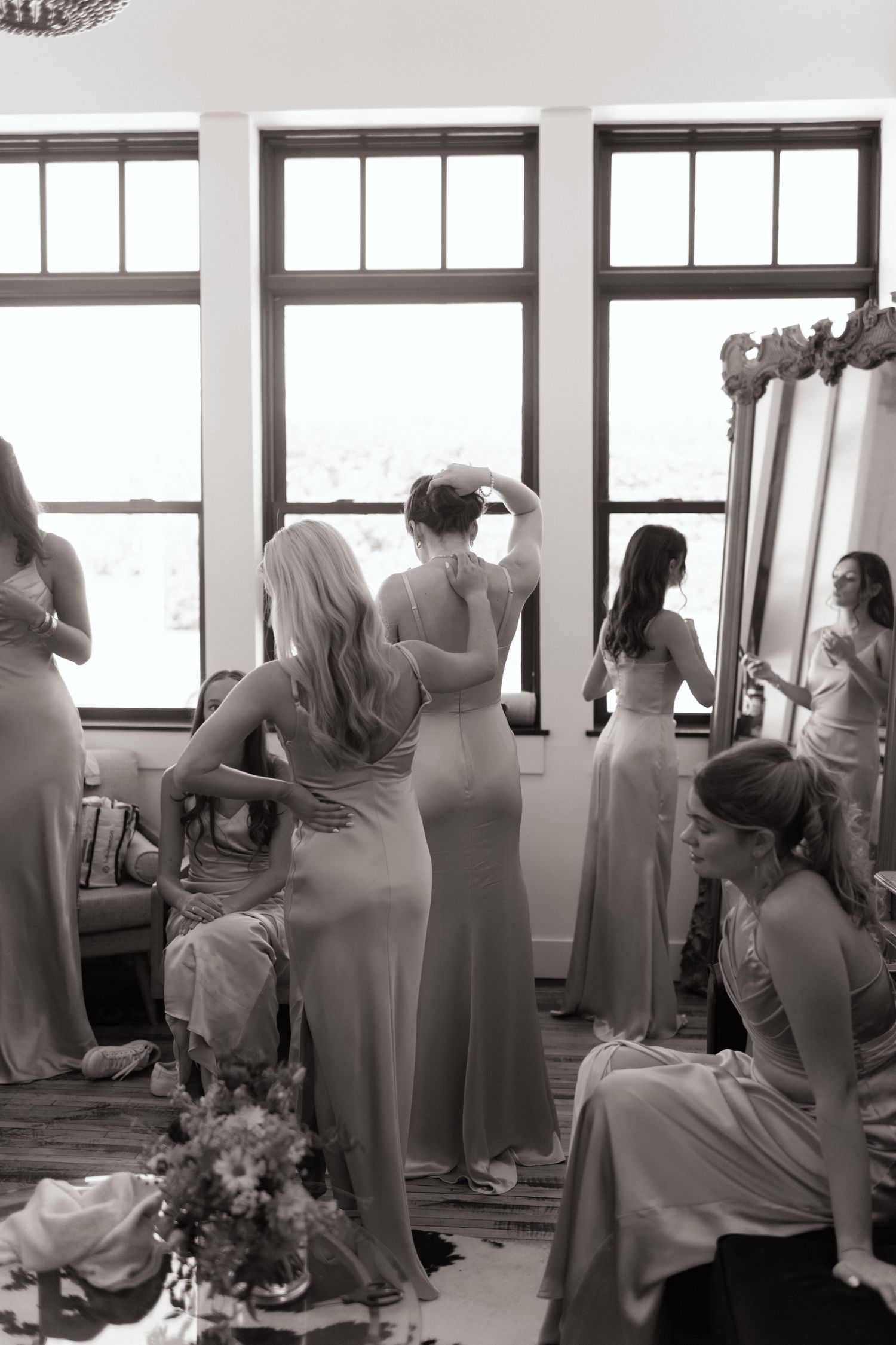 Wedding party in matching gowns preparing in bright room with large windows.