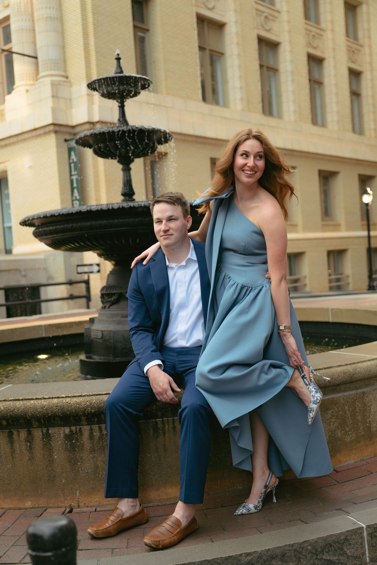 Couple in formal attire posing on stone steps near a historic building.