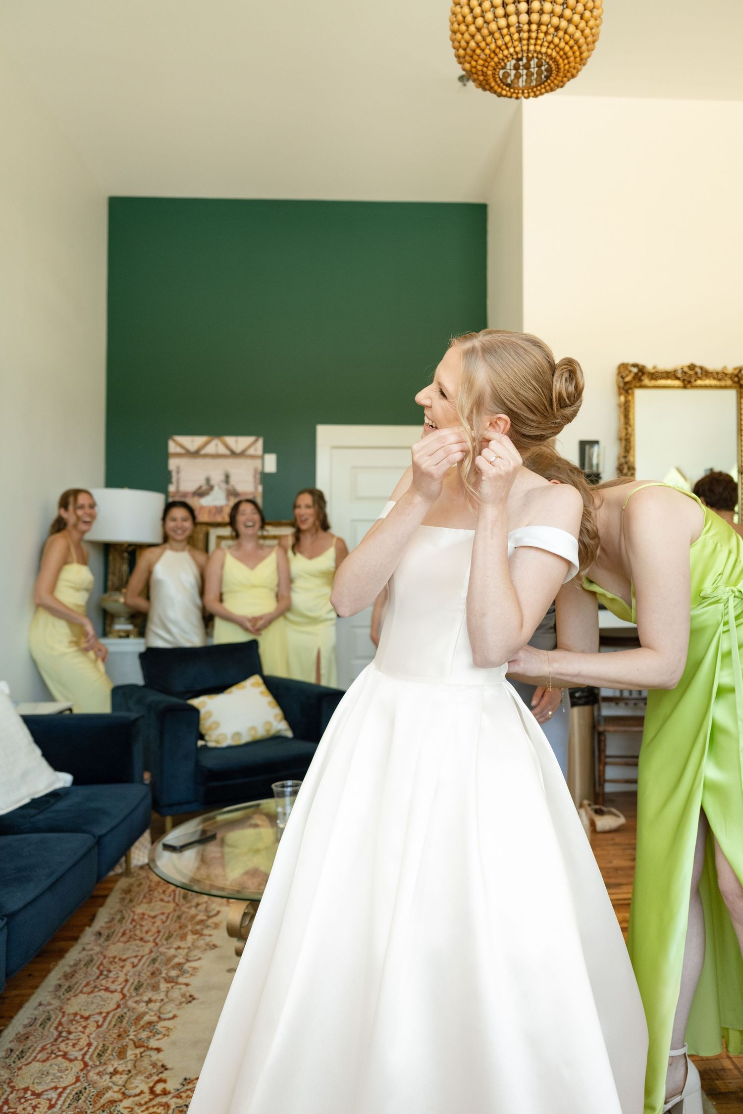 Bride getting ready in a room with bridesmaids in light green dresses and a disco ball overhead.