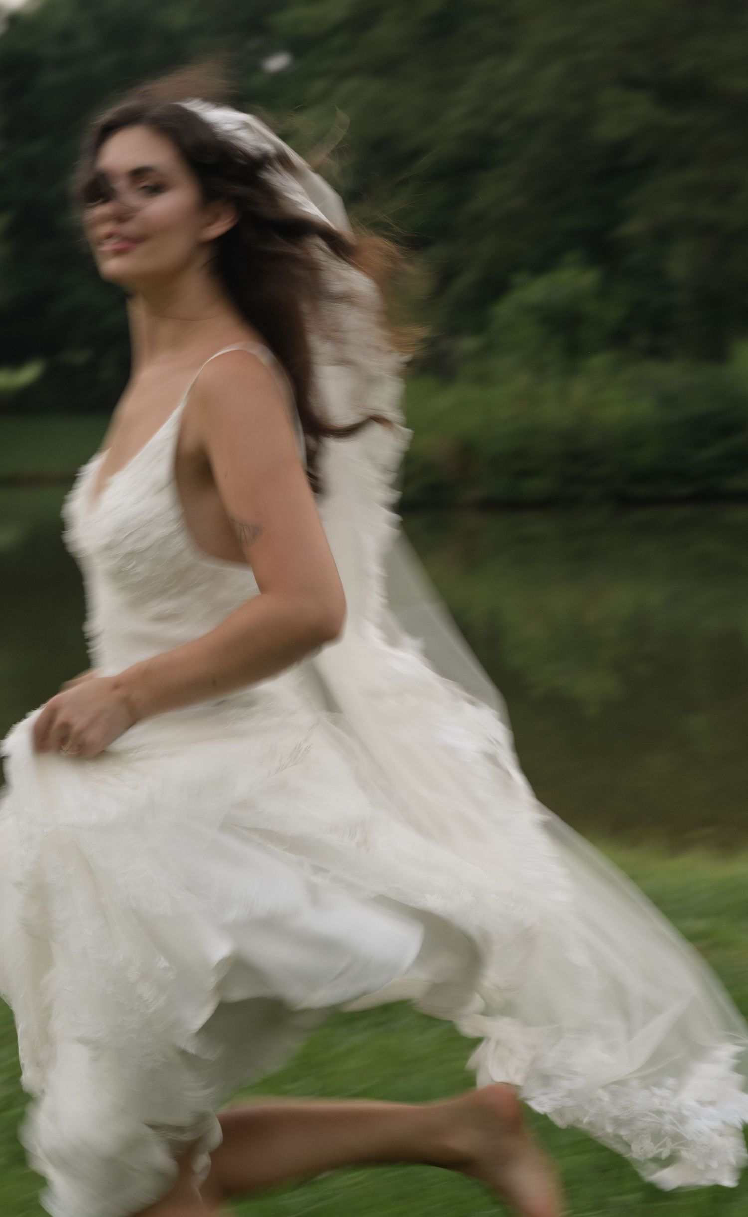 A flowing white wedding dress twirls gracefully in an outdoor setting with green foliage in the background.