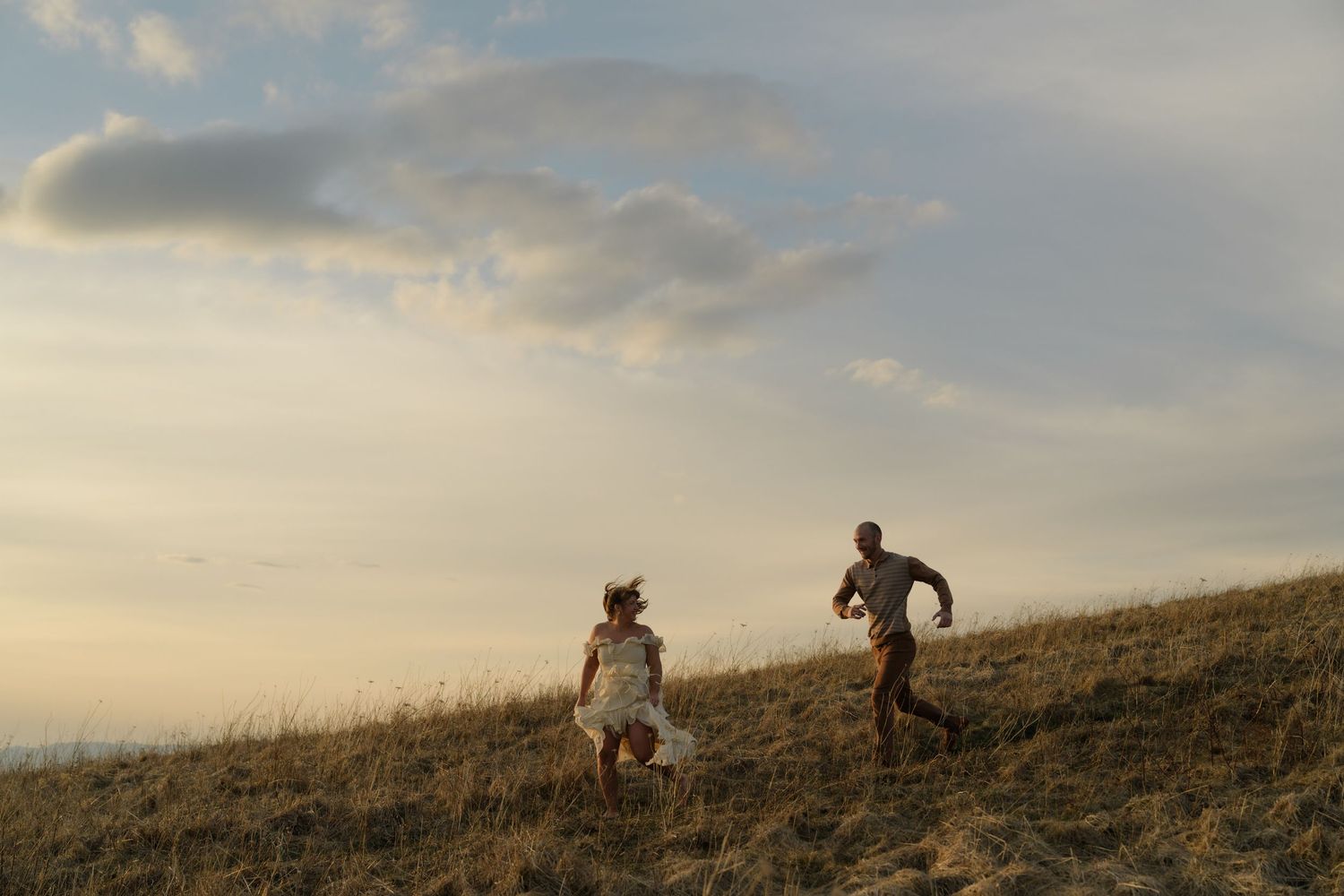 Two people hiking uphill during golden hour with dramatic clouds in the sky.