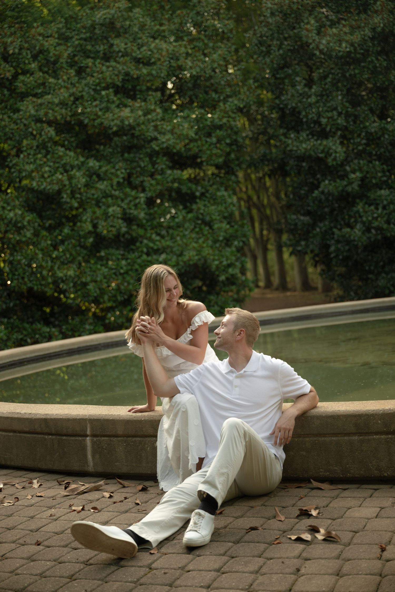 A couple in white clothing lying romantically on stone steps surrounded by lush greenery.