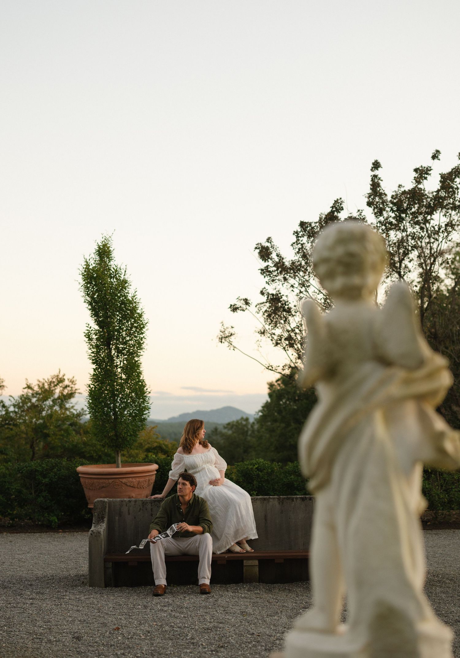 Artistic wedding scene with cherub statue in foreground at sunset.