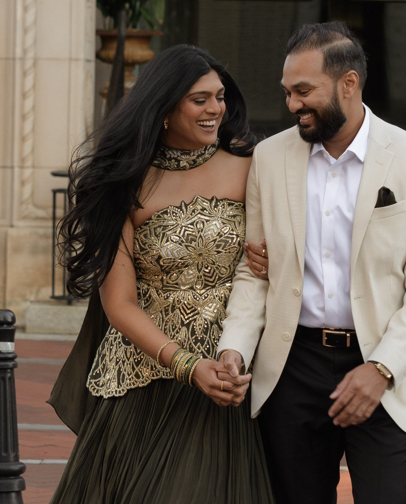 A couple shares a candid moment wearing elegant formal attire outside a classic building.