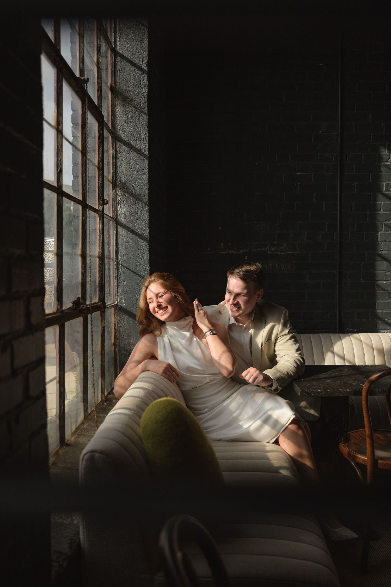 Couple relaxing together on leather couch in sunlit industrial space.