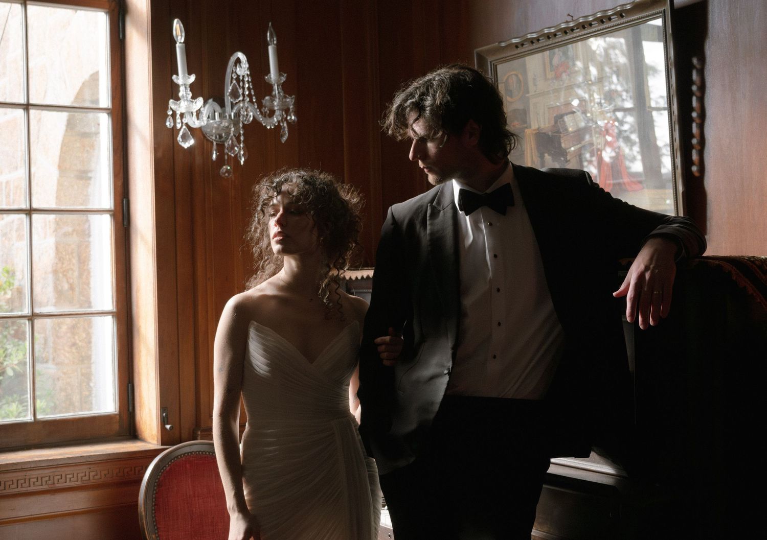 A couple dances together in an elegant room with chandeliers and large windows.