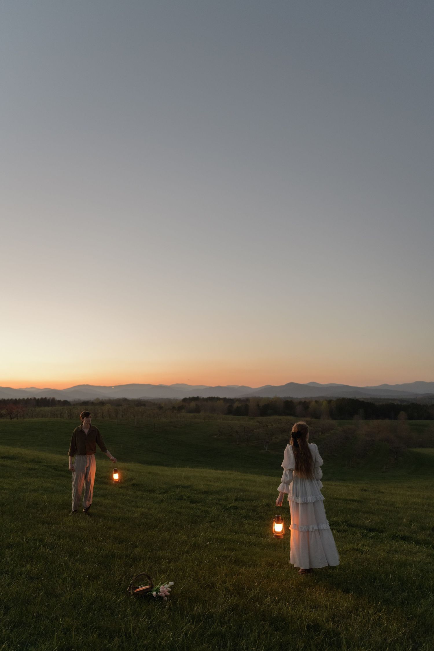 Silhouettes in a field at sunset with mountains in the distance and warm golden light.