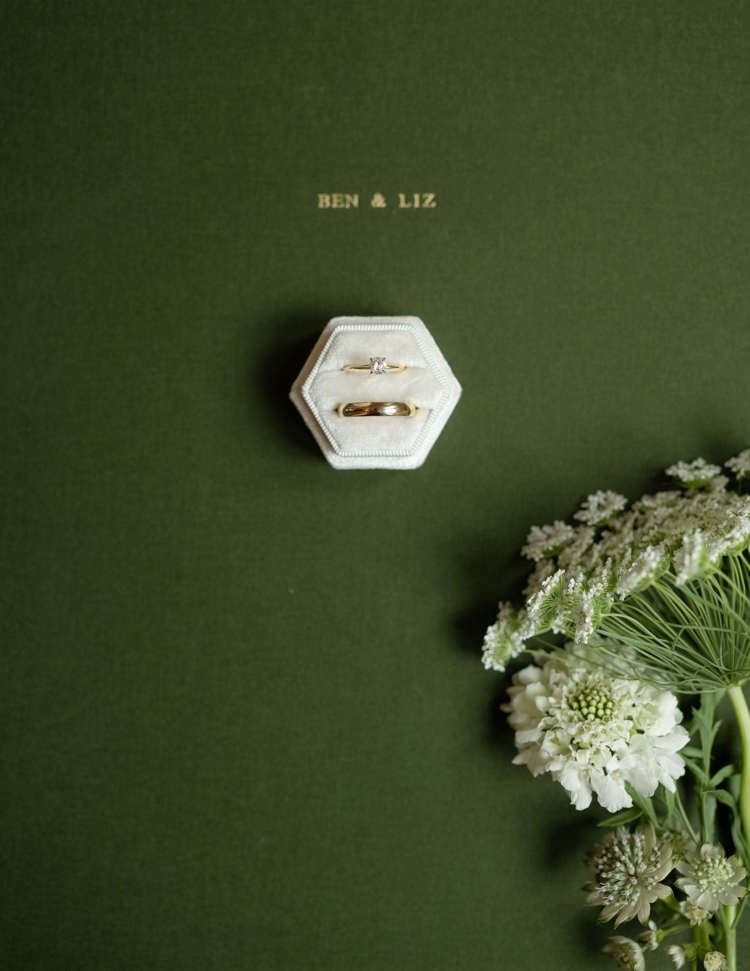 Minimalist wedding details photographed on dark green background with white florals.