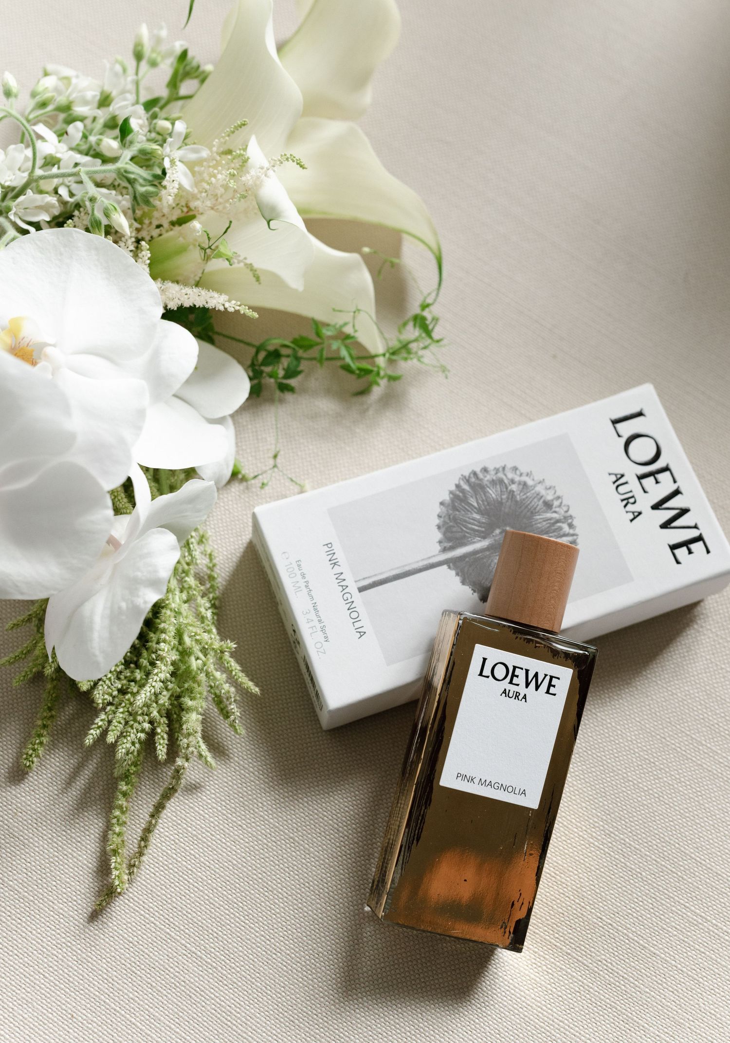 Elegant perfume bottles from Loewe displayed with delicate white flowers and greenery on a light textured surface.