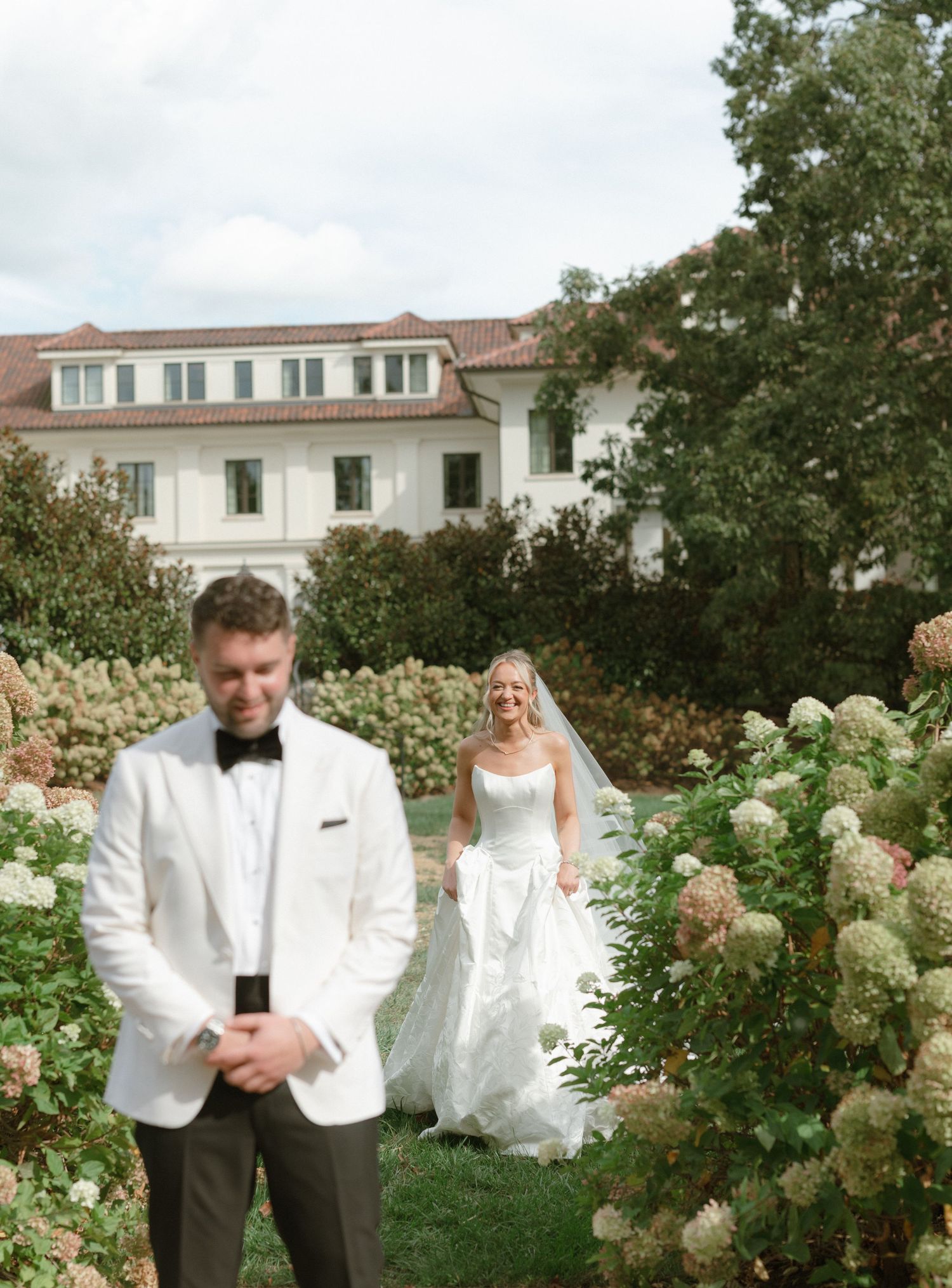 Wedding party poses in a lush garden setting with white hydrangeas and greenery creating a romantic backdrop.