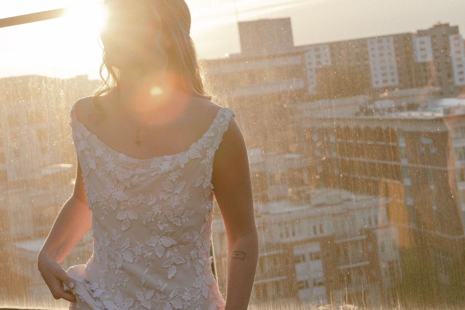 A person stands on a rooftop at sunset with a cityscape of buildings and golden light in the background.