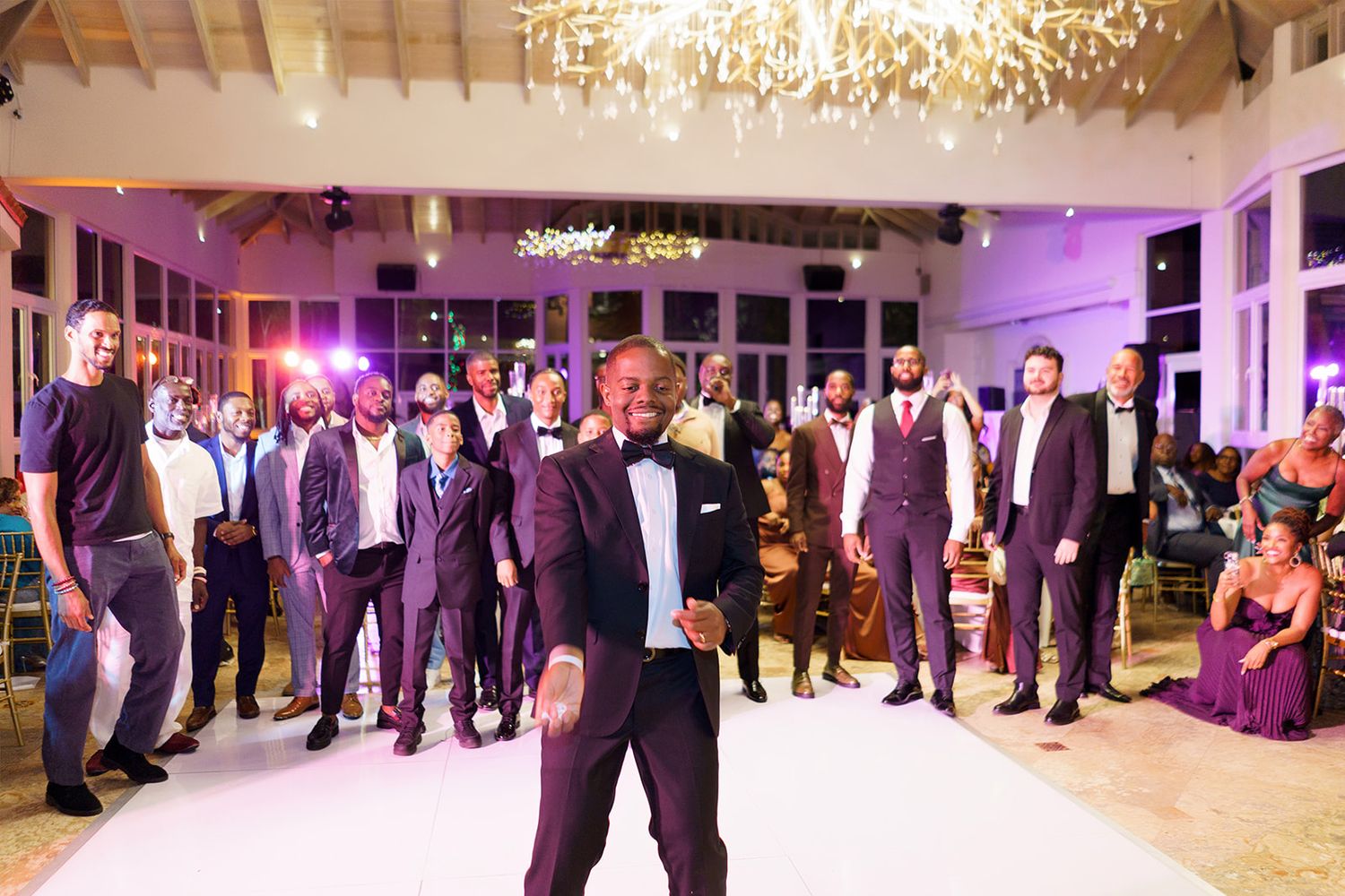 Groom stands on dance floor surrounded by groomsmen in purple suits at elegant wedding reception.