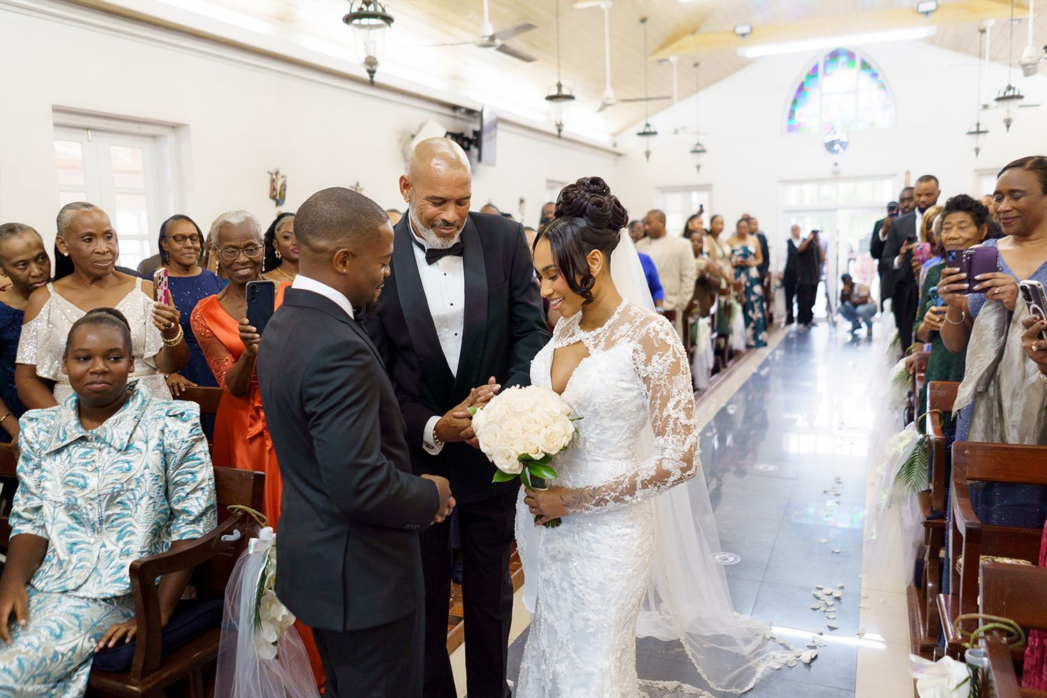 Bride in lace wedding dress exchanges rings with groom at church altar, surrounded by guests during wedding ceremony.