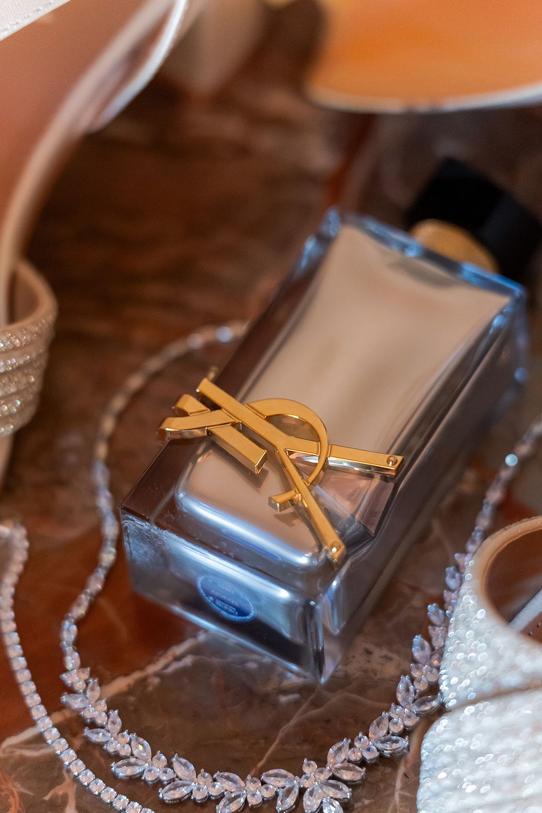 YSL Yves Saint Laurent perfume bottle with gold logo beside a diamond necklace on a marble surface.