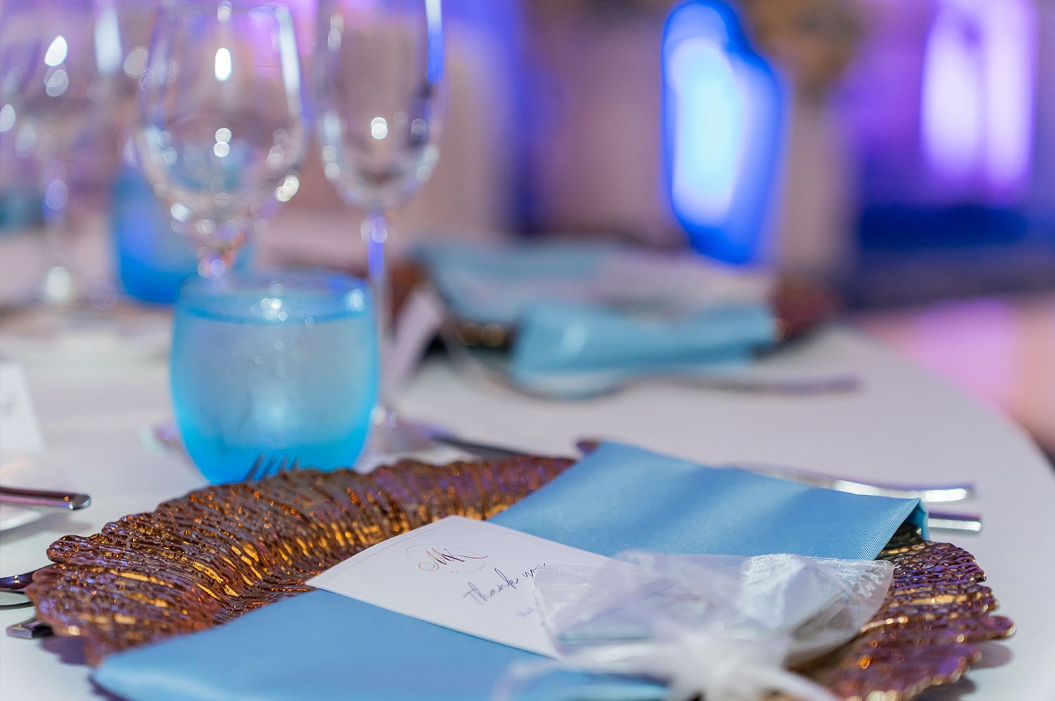 Elegant banquet table setting with blue napkins, crystal glasses, and decorative gold beaded charger plates.