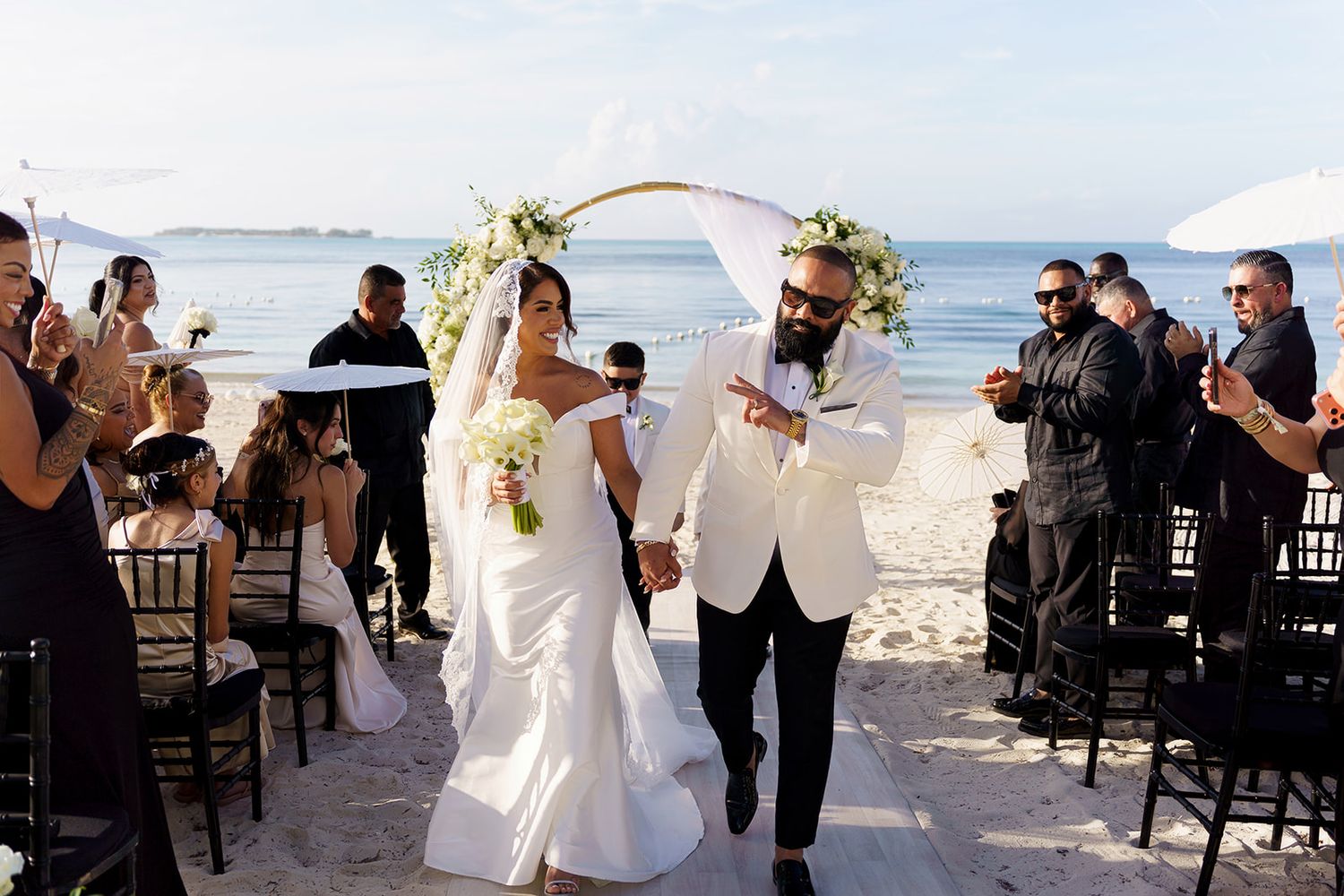 Bride and groom walk down sandy aisle at elegant beach wedding ceremony.