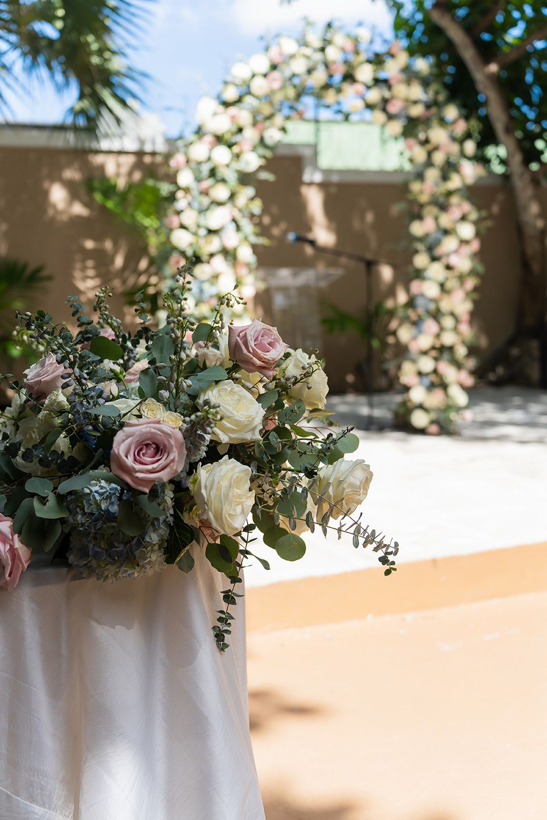 Elegant wedding ceremony floral arrangement with pink and white roses, greenery, and a floral arch in the background.