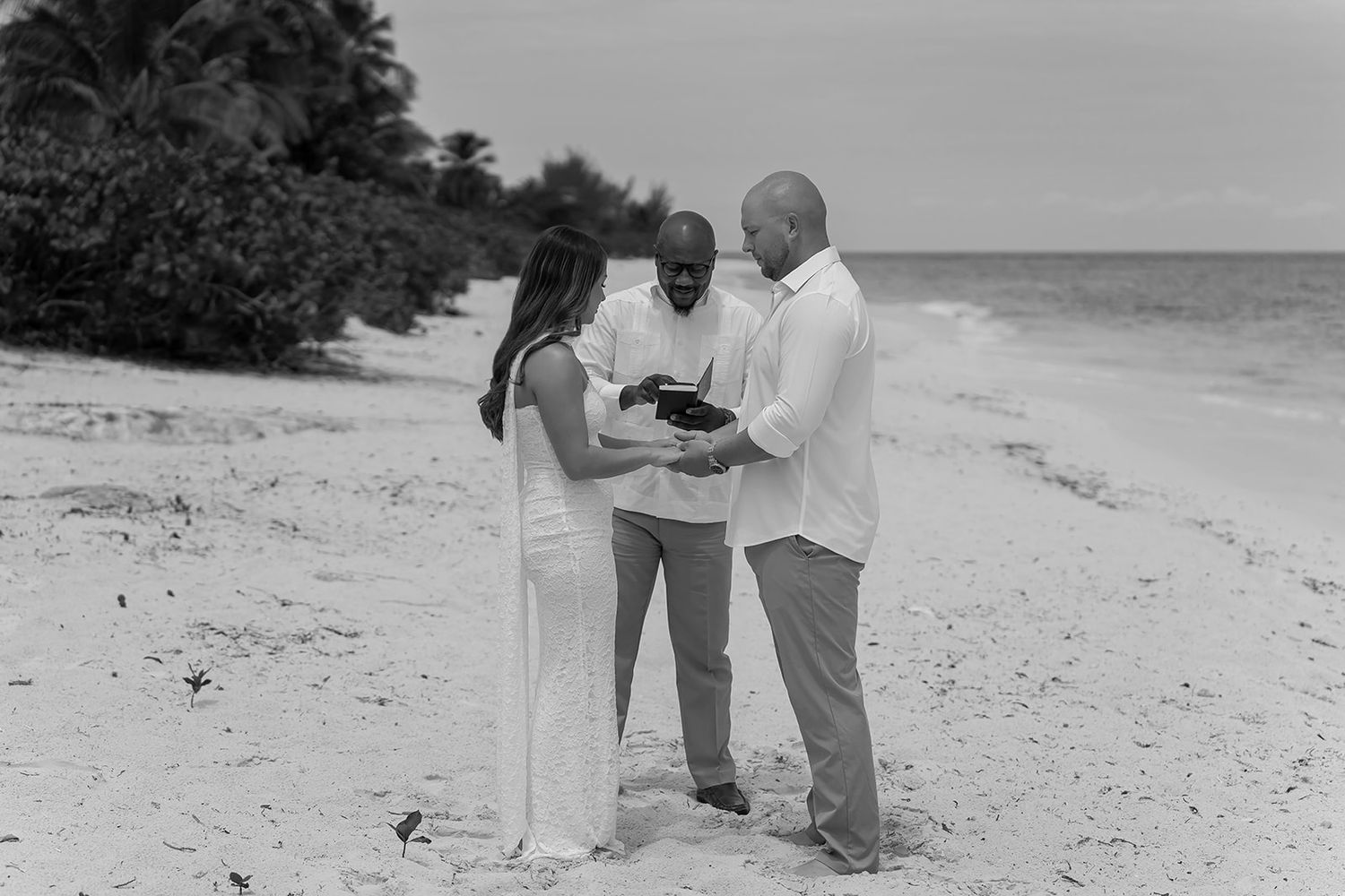 Black and white photo of couple exchanging vows with officiant on a tropical beach wedding ceremony.
