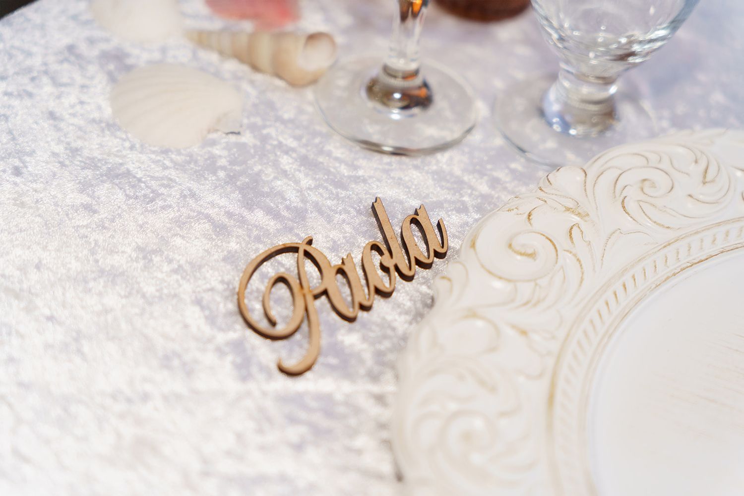 Elegant wooden laser-cut name place card on a decorative white wedding reception table setting.