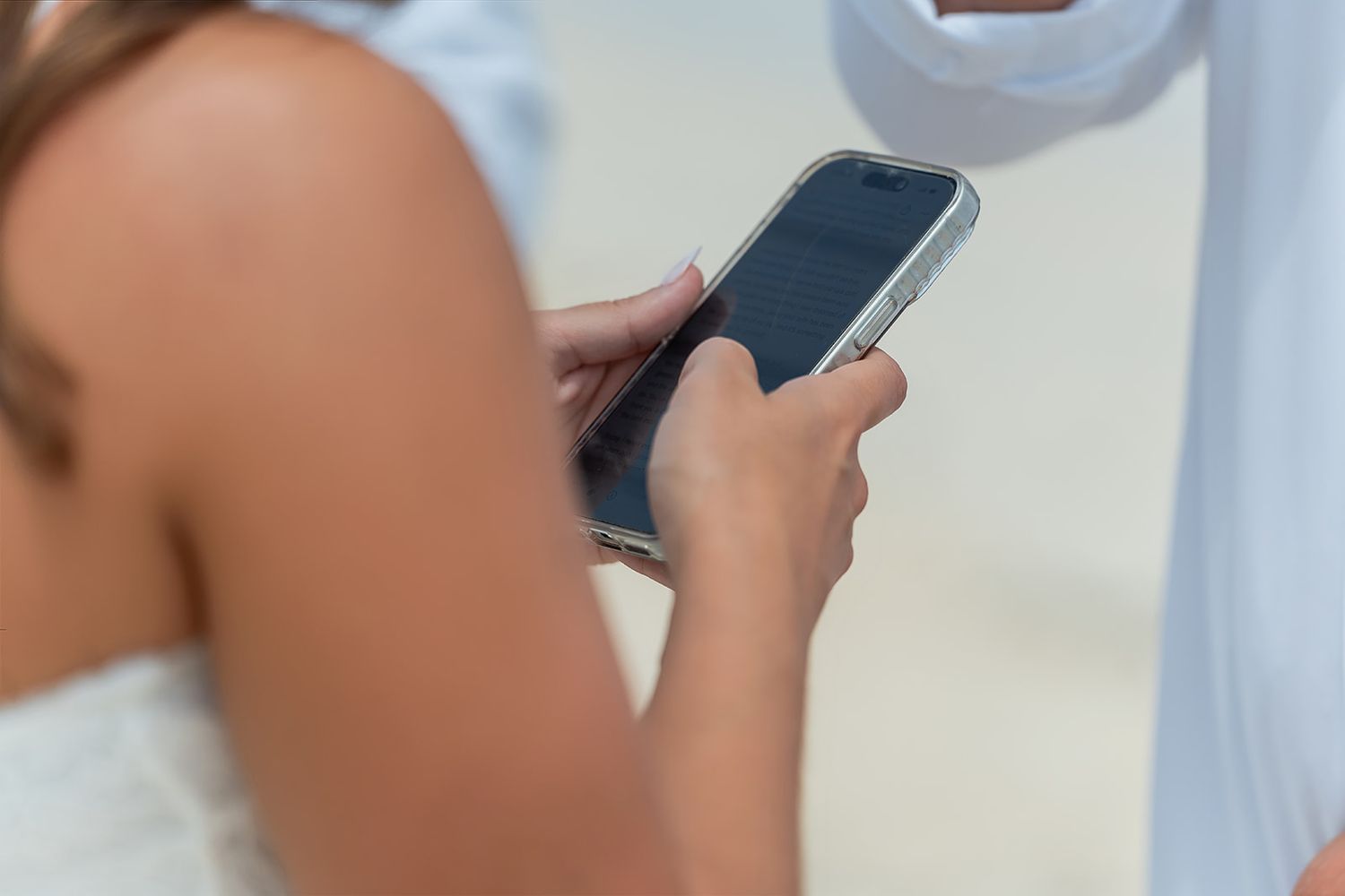 Close-up of a woman in white dress using a smartphone outdoors on a sunny day.