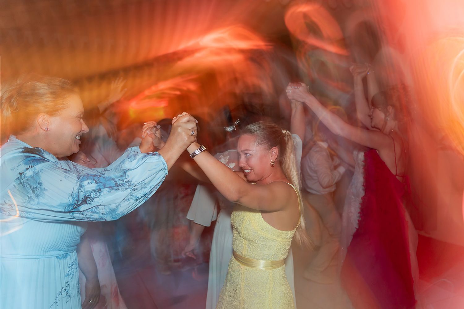 Women dancing joyfully at a wedding reception with colorful motion blur lights.