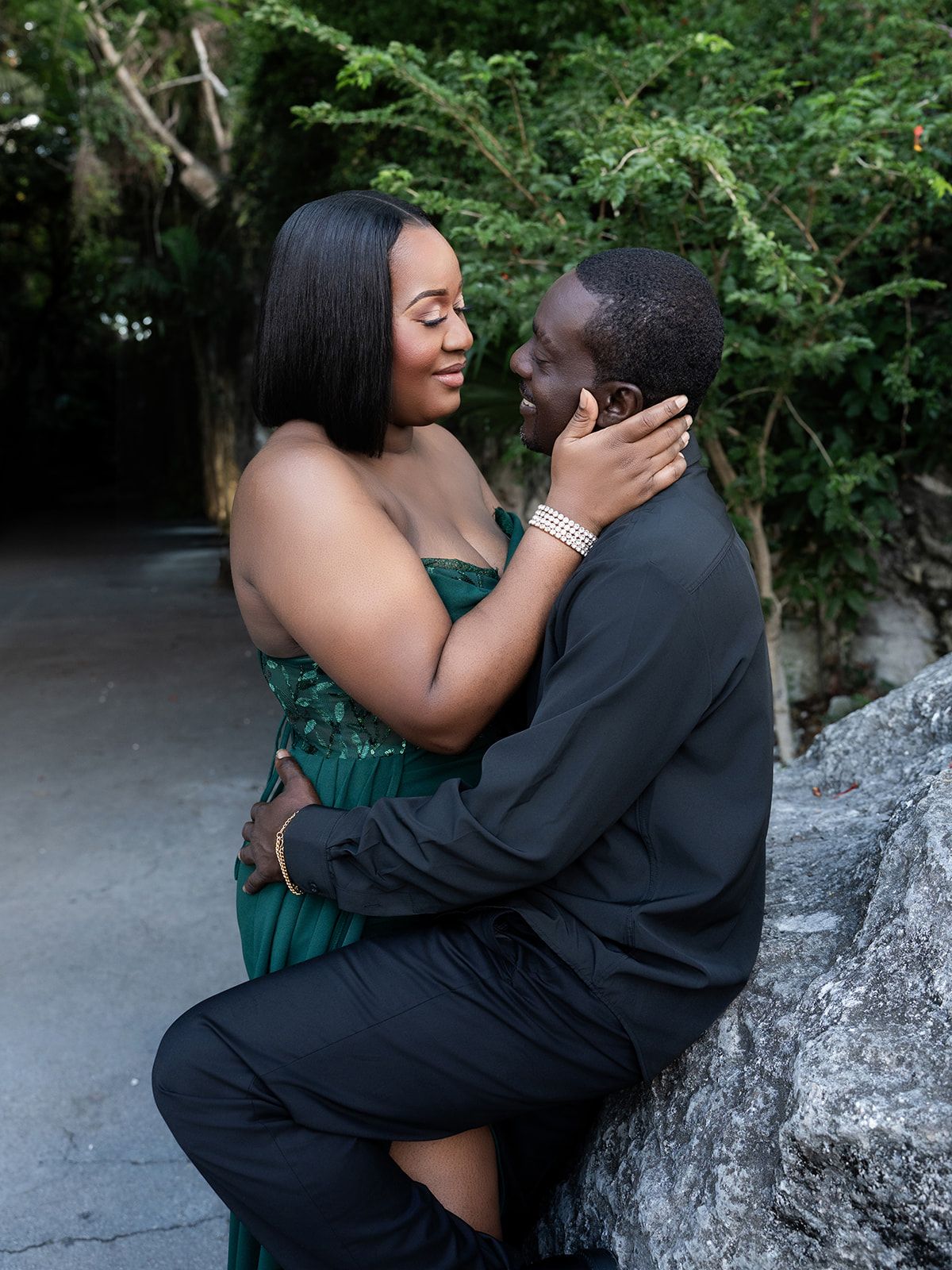 A couple in elegant formalwear shares a romantic moment outdoors, with the woman in green and man in black suit.