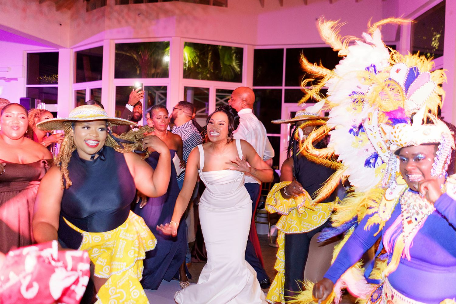 A bride celebrates with guests and a colorful costumed performer on the wedding reception dance floor.