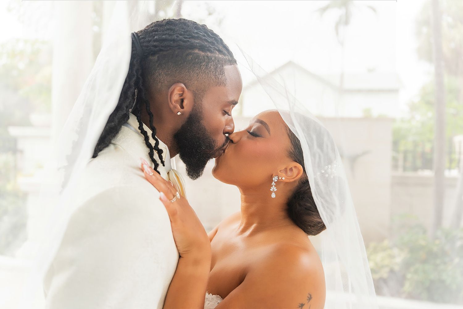 A couple shares a romantic kiss on their wedding day, bride in veil and groom in white suit.