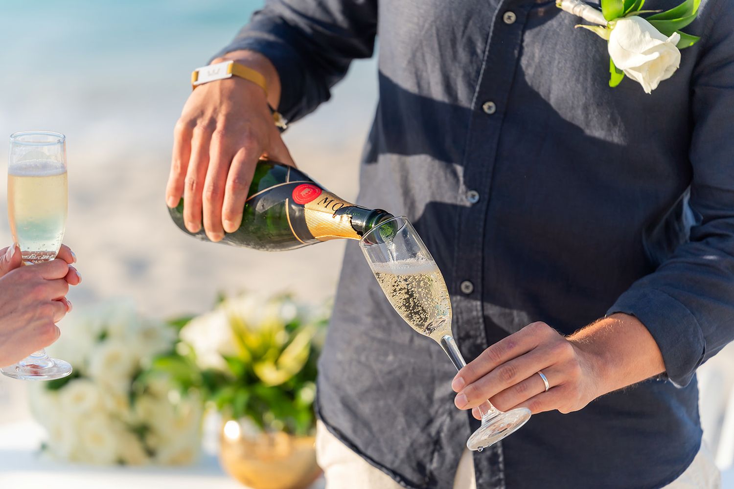 Groom pouring champagne into flute at beach wedding reception celebration.