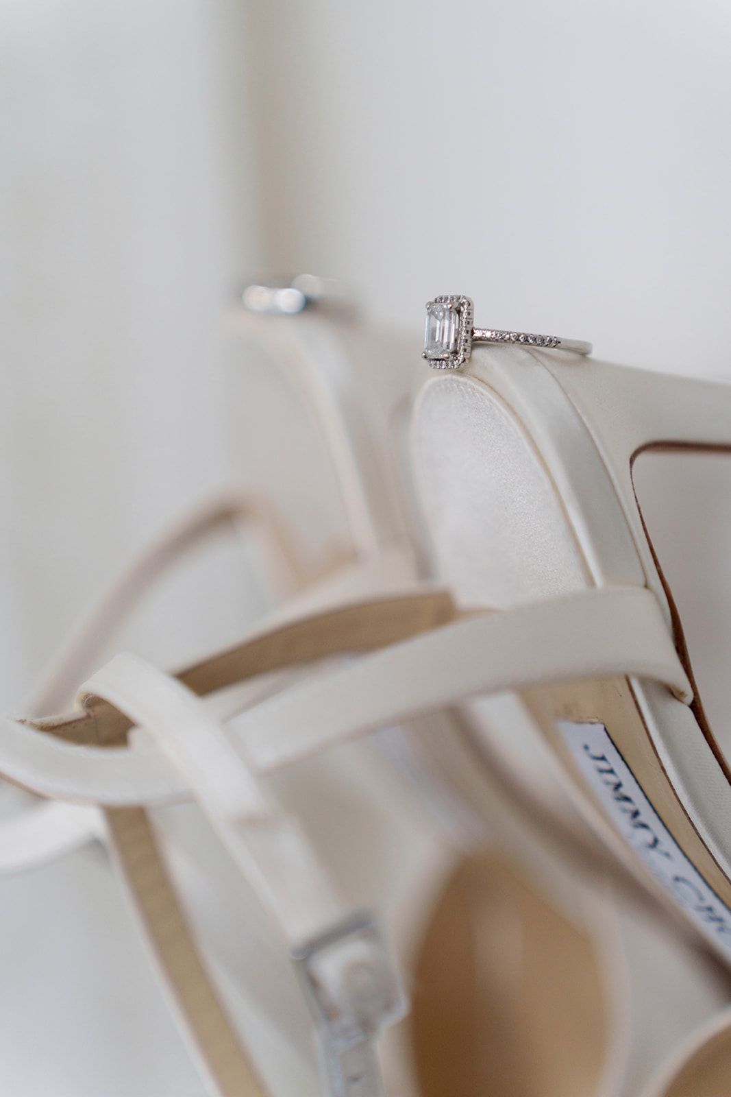 Elegant diamond engagement ring resting on ivory Jimmy Choo bridal heels, perfect wedding detail shot.