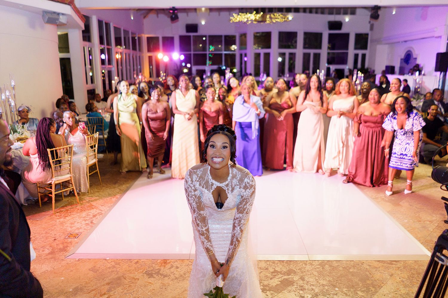 A bride prepares to toss her bouquet to excited bridesmaids lined up on the dance floor.
