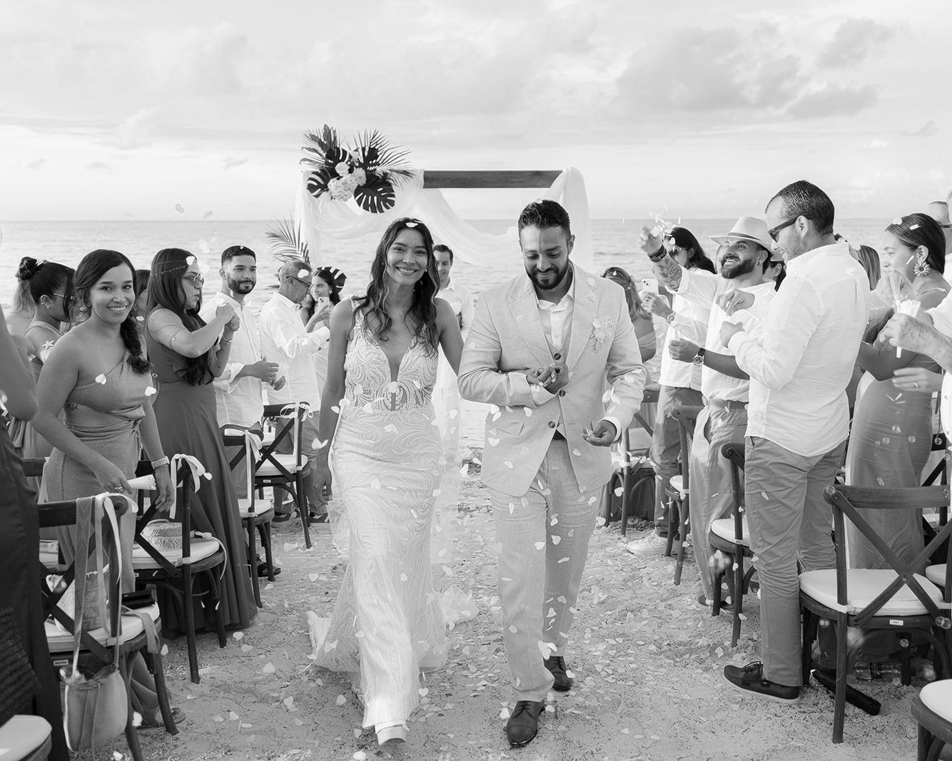 Black and white photo of a joyful couple walking down the aisle after their outdoor beach wedding ceremony.
