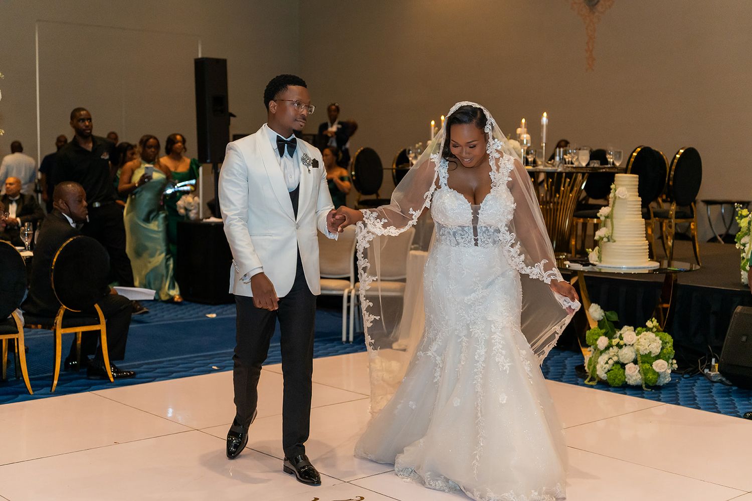 Bride and groom share first dance at elegant wedding reception with white dance floor and tiered cake.