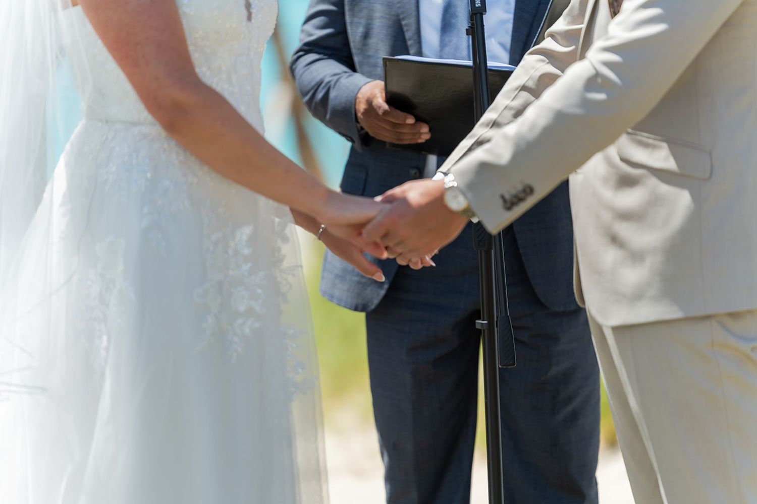 Bride and groom holding hands during outdoor wedding ceremony with officiant in background.