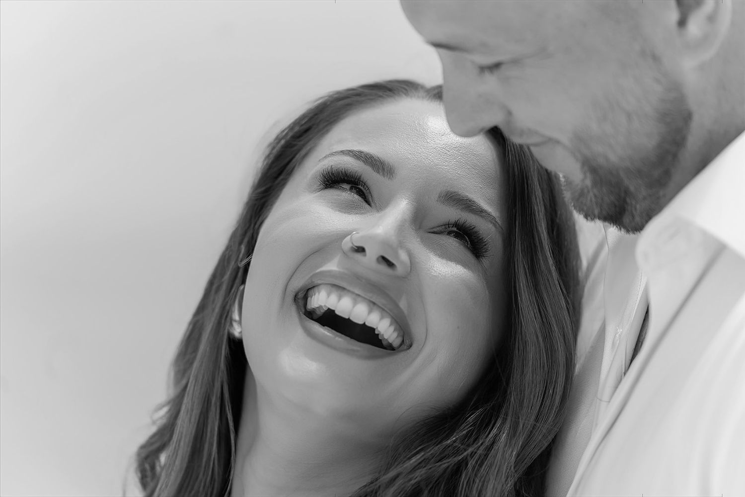 Black and white photo of a laughing woman and smiling man sharing a joyful, intimate moment together.