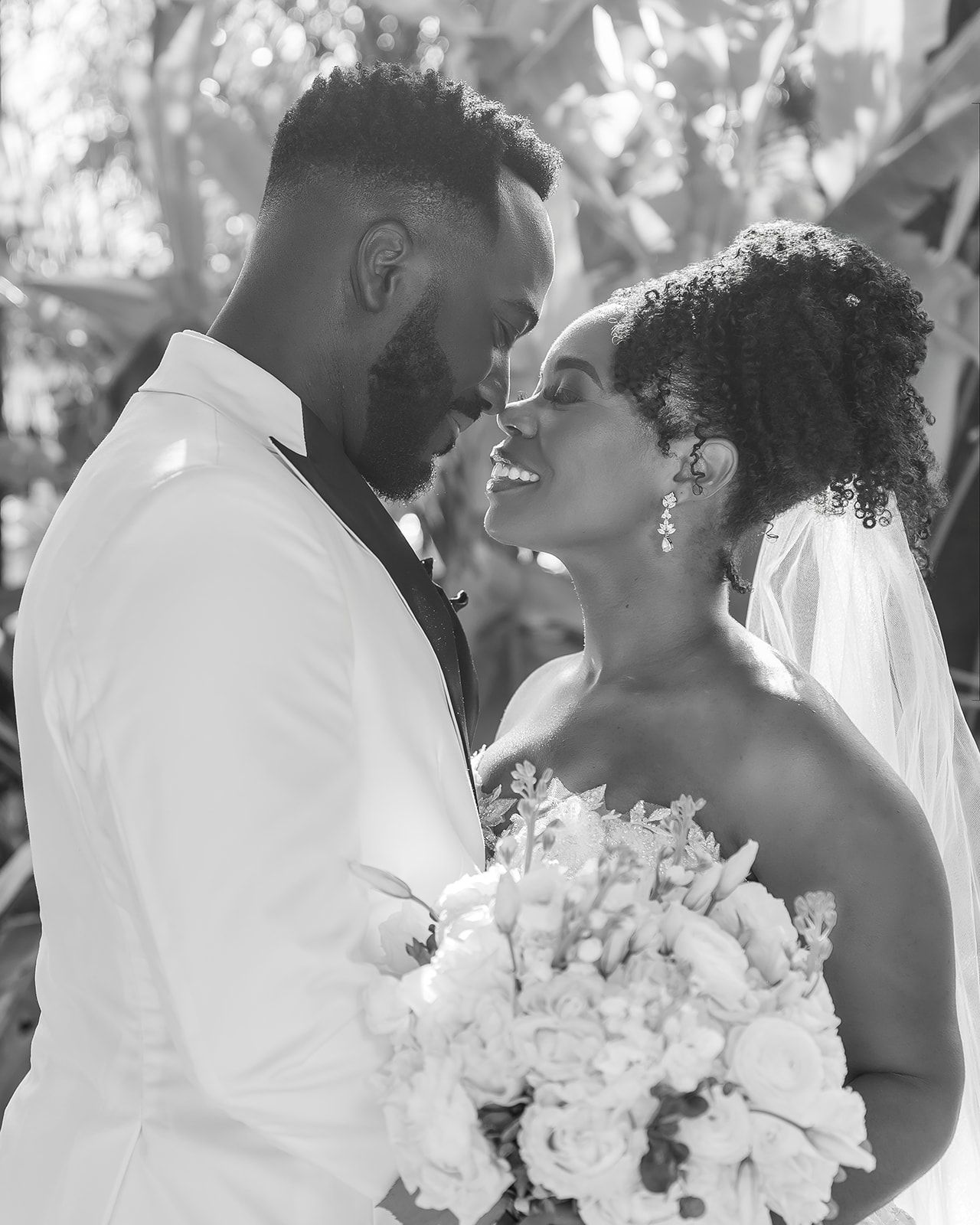 Black and white wedding photo of a smiling bride and groom in an intimate moment, bride holding a bouquet.