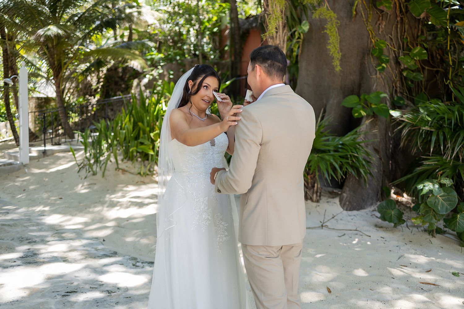 Bride and groom share a tender moment during outdoor beach wedding ceremony surrounded by lush tropical greenery.