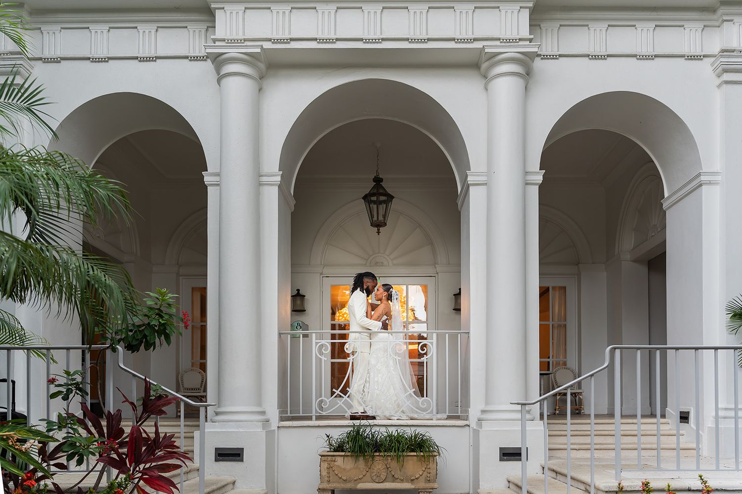 Bride and groom share a romantic kiss under white arched columns of an elegant venue.