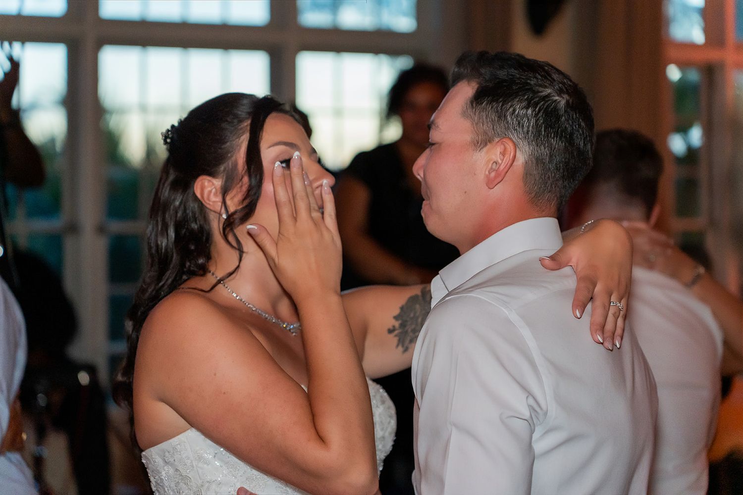 Emotional bride wiping tears during first dance with groom at wedding reception.