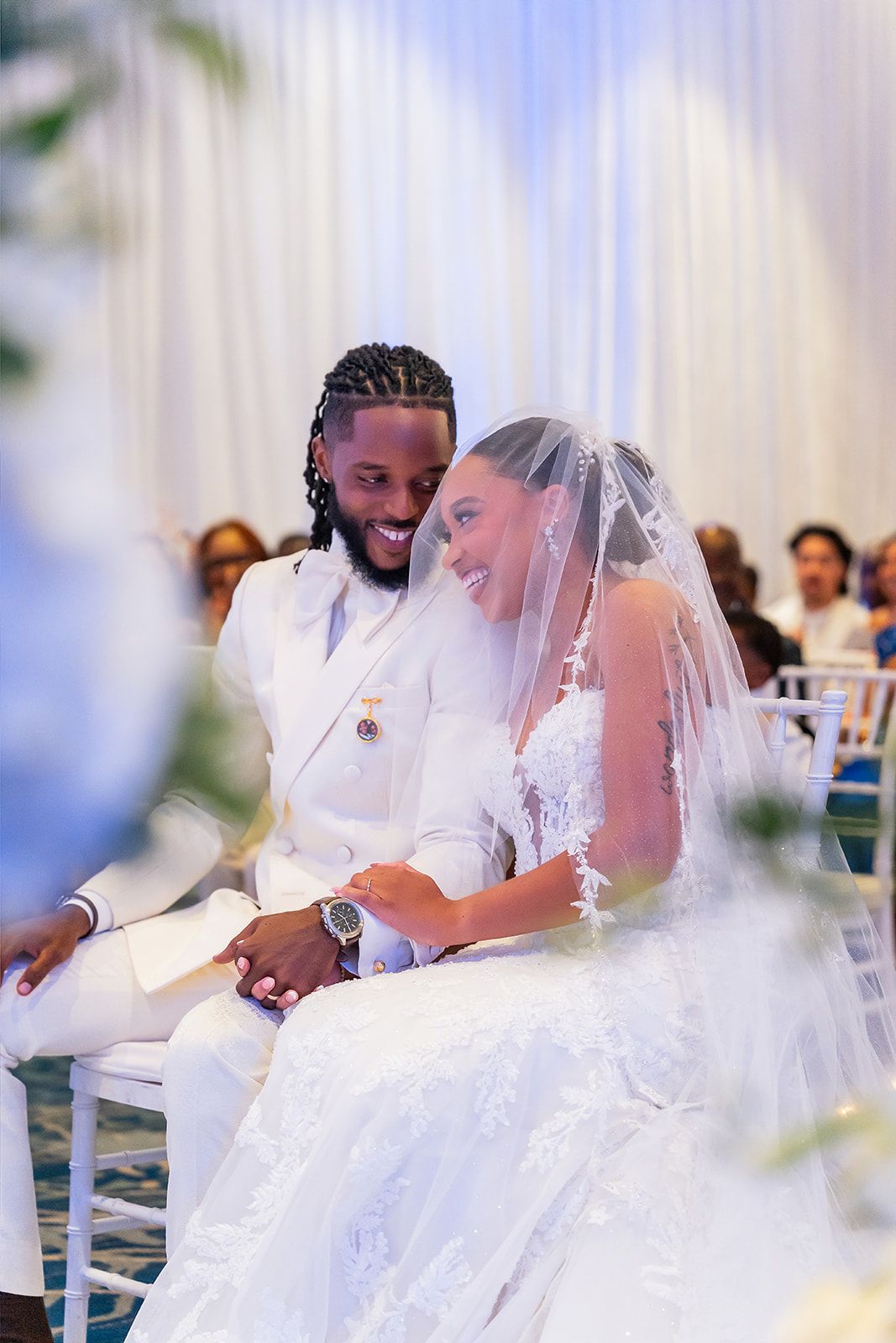 Smiling bride and groom in white attire share a joyful moment during their elegant wedding ceremony.