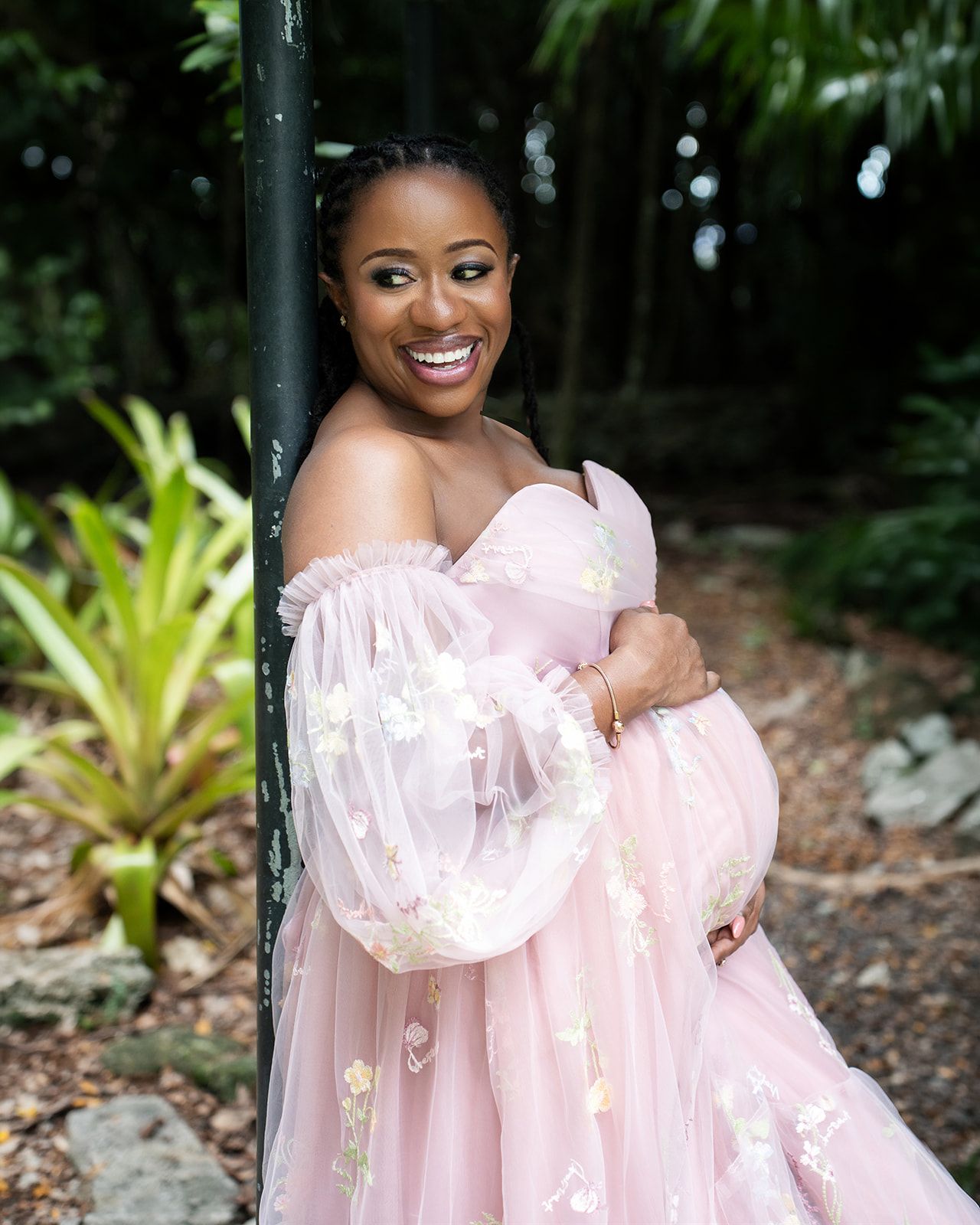 Pregnant woman in a pink dress surrounded by lush greenery