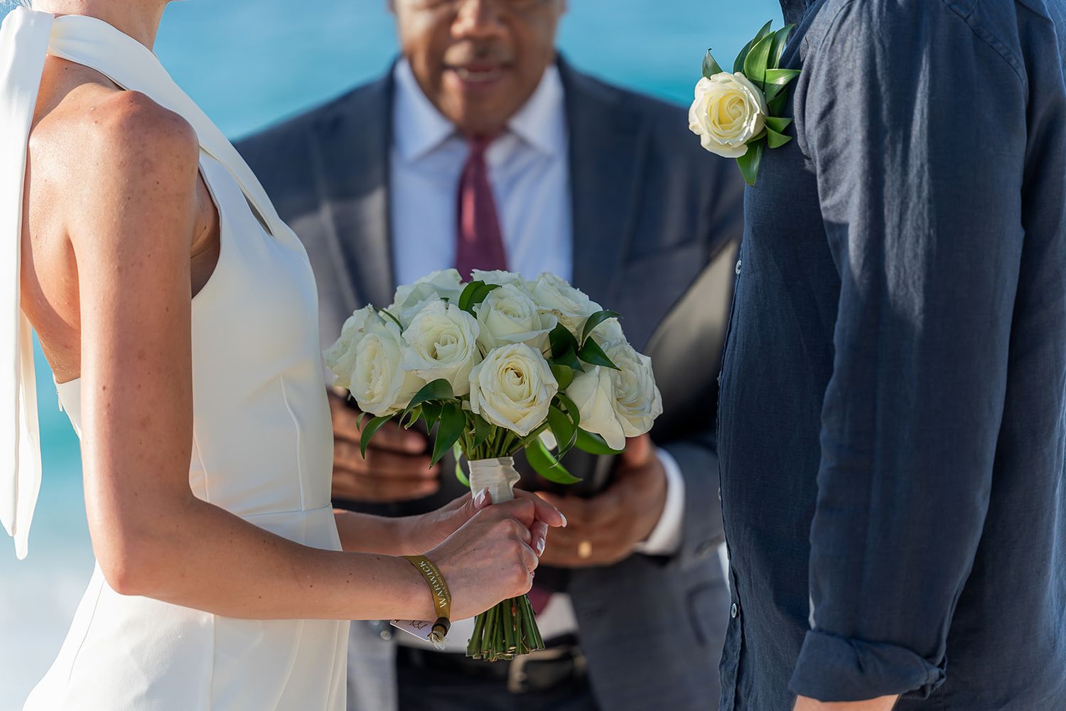 Bride and groom exchanging vows with officiant at outdoor waterfront wedding ceremony.